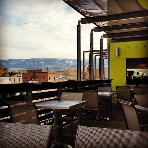 A rooftop patio with empty tables overlooking mountains and a town, under a cloudy sky.