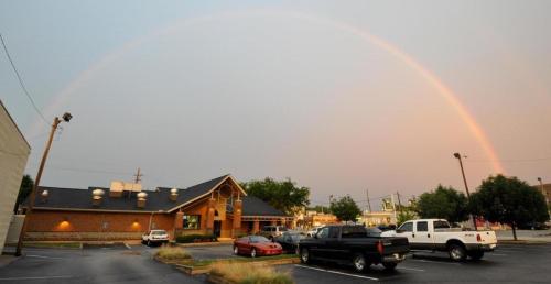 A rainbow arcs over a parking lot with a restaurant and cars, under a cloudy sky.