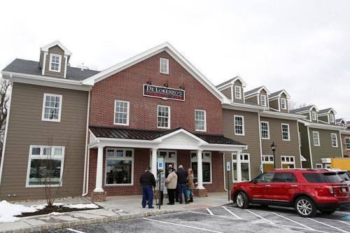 A brick restaurant building with a sign reading "De Lorenzo's," featuring a group of people waiting outside.