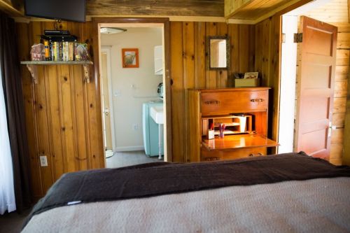 Cozy wooden room with a bed, a desk, and a doorway leading to a laundry area. Natural light filters in.