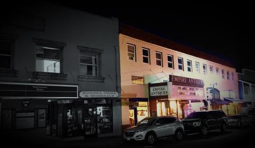 Nighttime view of a street with antique shops and a gem store, illuminated by colorful lights.