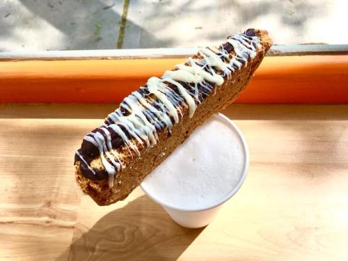 A long biscotti drizzled with chocolate and white icing rests on a cup of frothy coffee.