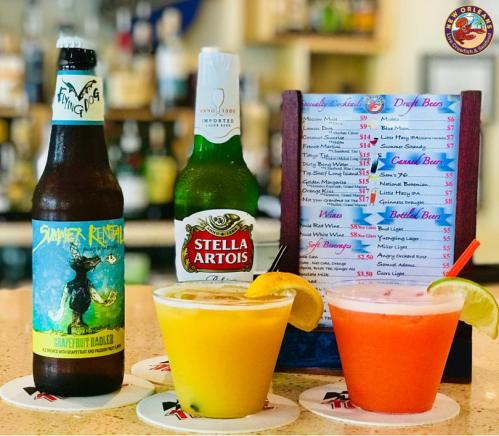 A colorful display of drinks: two cocktails with lemon slices, a Flying Dog beer, and a Stella Artois on a bar counter.