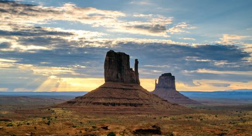 A scenic view of Monument Valley with towering rock formations under a dramatic sky at sunset.