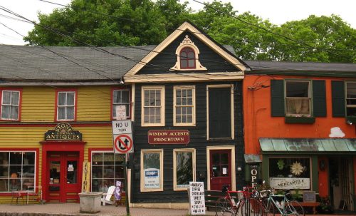 Colorful storefronts line a street, featuring antique shops and a cafe, with trees and power lines in the background.