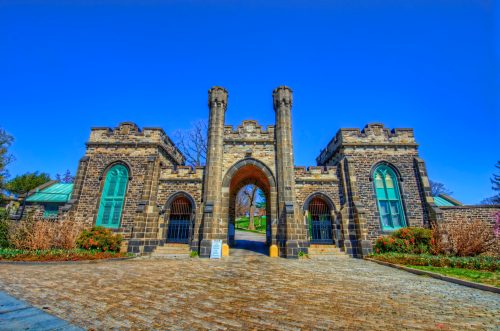 Historic stone gate with towers and arched entrance, surrounded by greenery and blue sky.