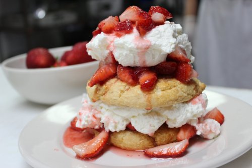 A tall dessert of layered biscuits, whipped cream, and fresh strawberries drizzled with strawberry sauce.
