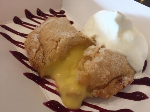 A dessert featuring a golden, sugar-coated pastry filled with creamy lemon curd, served with a scoop of vanilla ice cream.