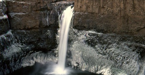 A majestic waterfall cascading down rocky cliffs into a serene pool below, surrounded by textured stone formations.