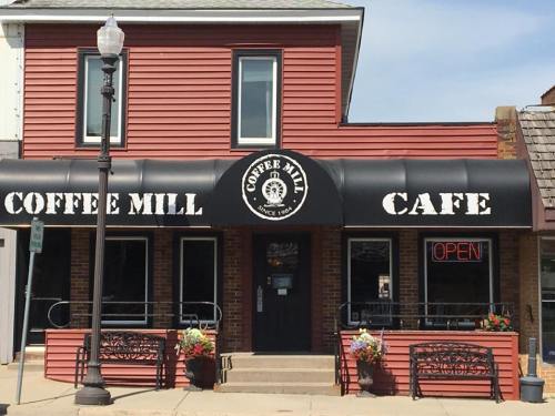 A red building with a black awning reading "Coffee Mill Cafe," featuring outdoor seating and an "Open" sign.