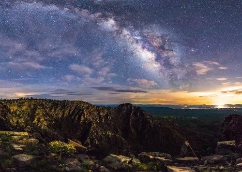 A stunning night sky filled with stars and the Milky Way over a mountainous landscape at dusk.