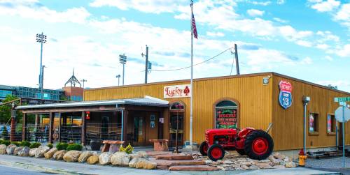 A rustic wooden building with a red tractor in front, featuring a sign that reads "Lucky" and an American flag.