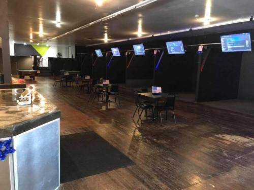 Interior of a spacious venue with tables, chairs, and multiple screens, featuring a dark color scheme and American flags.