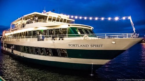 A large boat named "Portland Spirit" docked at night, illuminated by string lights on the water.