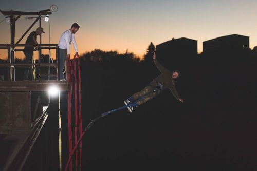 A person bungee jumping off a platform at sunset, with onlookers watching from above.
