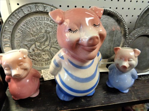 Three ceramic pig figurines in pastel colors, with one larger pig wearing a striped shirt and two smaller pigs beside it.
