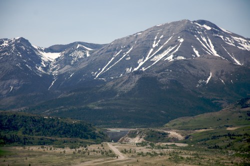 A scenic view of snow-capped mountains with a valley and a winding road in the foreground under a clear blue sky.