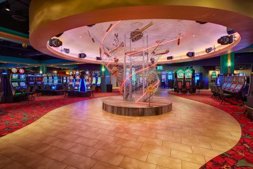 A vibrant casino interior featuring slot machines, colorful carpet, and a central artistic installation.