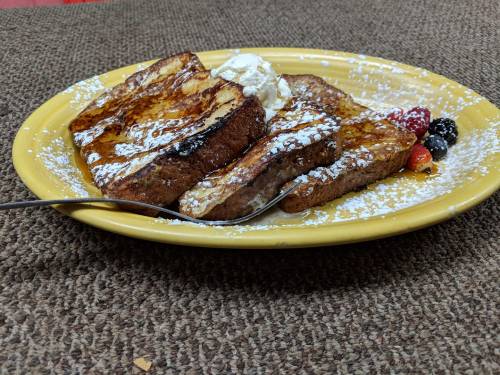 A plate of French toast topped with powdered sugar, whipped cream, and mixed berries on a textured surface.