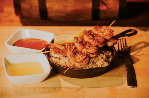 Grilled shrimp skewers on rice, served with lemon wedges and two dipping sauces in small bowls.