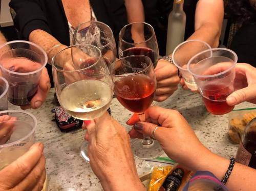 A group of hands holding various glasses and cups, toasting with drinks in a festive setting.