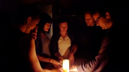A group of five people gathered around a candle in a dimly lit room, engaged in a focused activity.