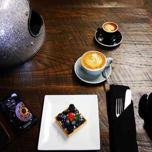 A stylish table setting with a helmet, two coffee cups, a smartphone, and a dessert topped with berries.