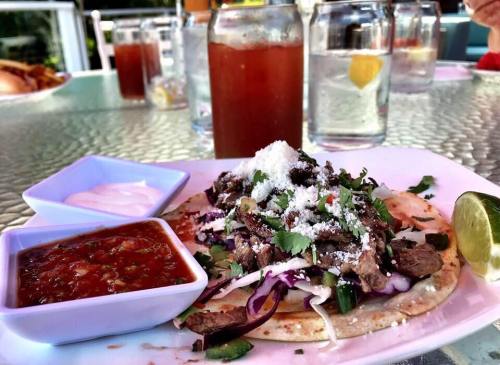 A plate of tacos topped with beef, cheese, and cilantro, served with salsa and a lime wedge, with drinks in the background.