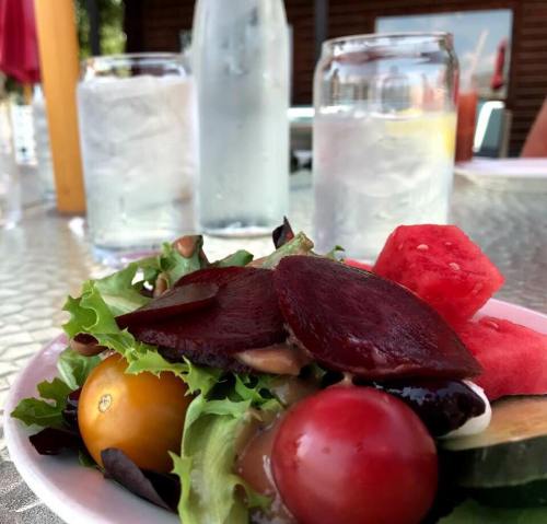 A fresh salad with beets, cherry tomatoes, and watermelon, with glasses of water in the background.