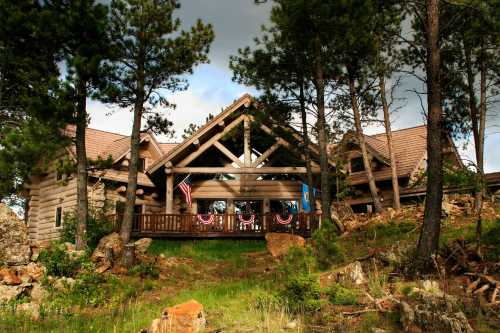 A rustic log cabin surrounded by trees, featuring a porch with patriotic decorations and a scenic hillside.