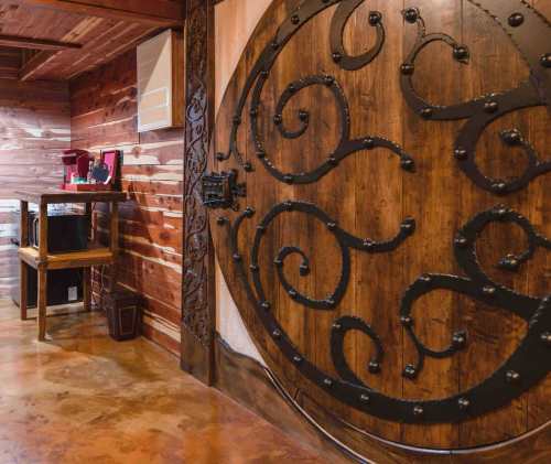 A large, ornate wooden door with decorative metalwork, set in a rustic interior with wooden walls and a small table.