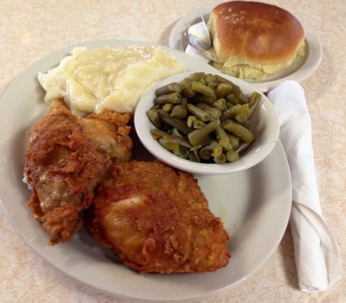 A plate of fried chicken with mashed potatoes, green beans, and a roll, served with a napkin on the side.