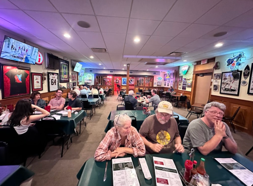 A cozy restaurant interior with patrons at tables, sports memorabilia on the walls, and a warm, inviting atmosphere.