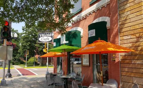 A quaint café with green and orange umbrellas outside, located on a sunny street corner with traffic lights.