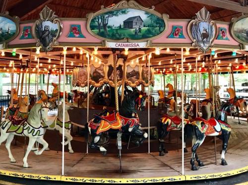 A vintage carousel with intricately painted horses and colorful lights, set in a charming wooden pavilion.