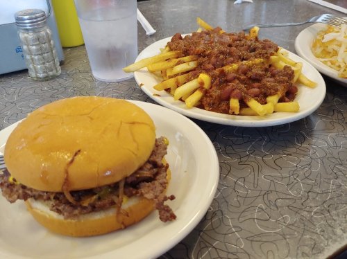 A plate with a burger and a side of chili cheese fries on a retro-style table.