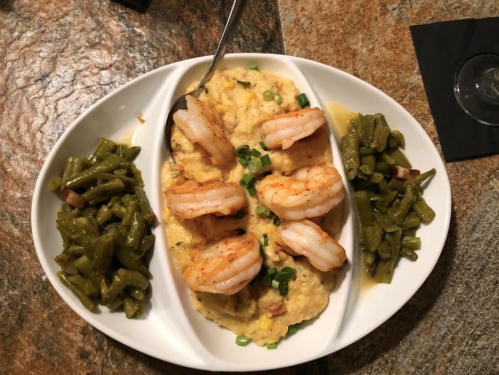 A plate of shrimp and grits topped with green onions, flanked by two servings of green beans.