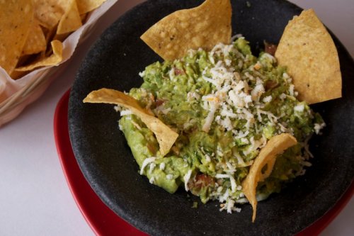 A bowl of guacamole topped with cheese and tortilla chips, served with a side of crispy tortilla chips.