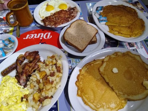 A hearty breakfast spread featuring eggs, bacon, pancakes, toast, and hash browns on a table.