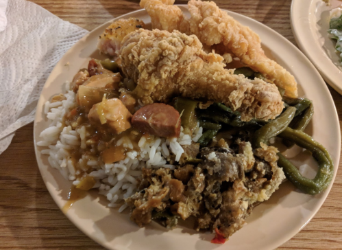 A plate of food featuring fried chicken, rice with sausage, green beans, and a side of mixed vegetables.