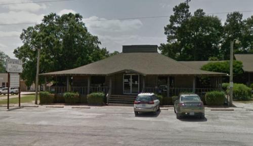 A single-story building with a sloped roof, surrounded by trees and parked cars, likely a restaurant or family gathering place.