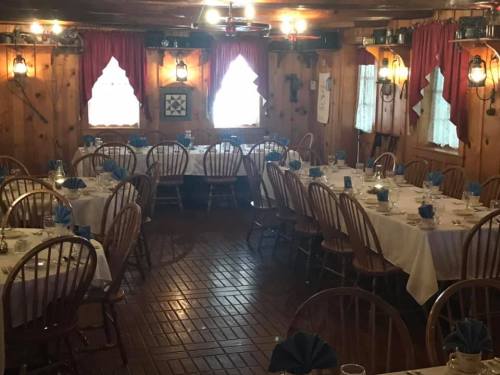 Cozy dining room with wooden walls, tables set with white tablecloths and blue napkins, and warm lighting.