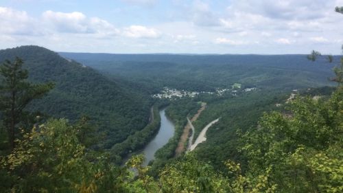 A scenic view of rolling green hills and a winding river under a partly cloudy sky.
