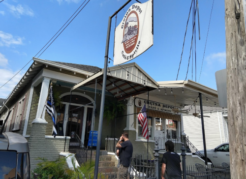 A historic building with a sign reading "Crescent Depot," featuring flags and outdoor seating under a blue sky.