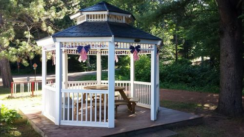 A white gazebo with a black roof, featuring a picnic table inside and decorated with small American flags.