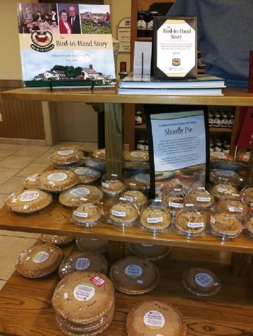 A display of Shoofly pies and books about Bird-in-Hand, featuring a table with various baked goods and informational signage.