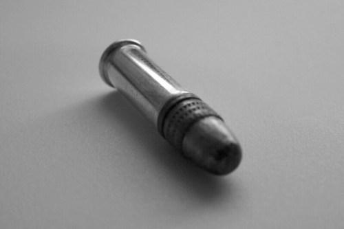 A close-up of a metallic bullet lying on a flat surface, captured in black and white.