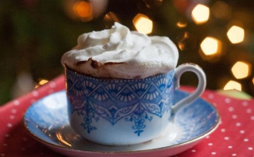 A decorative cup filled with hot chocolate topped with whipped cream, set on a plate with a festive background.