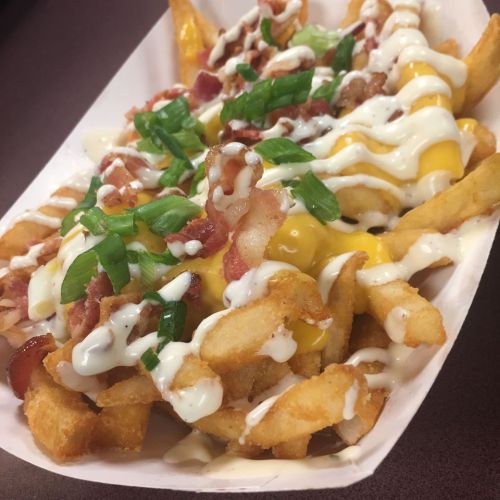 A tray of loaded fries topped with cheese, bacon, green onions, and drizzled with sauce.