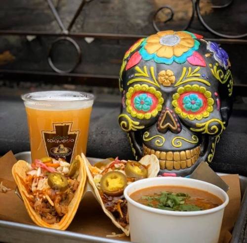 A colorful sugar skull centerpiece with tacos, jalapeños, and a beer on a tray.